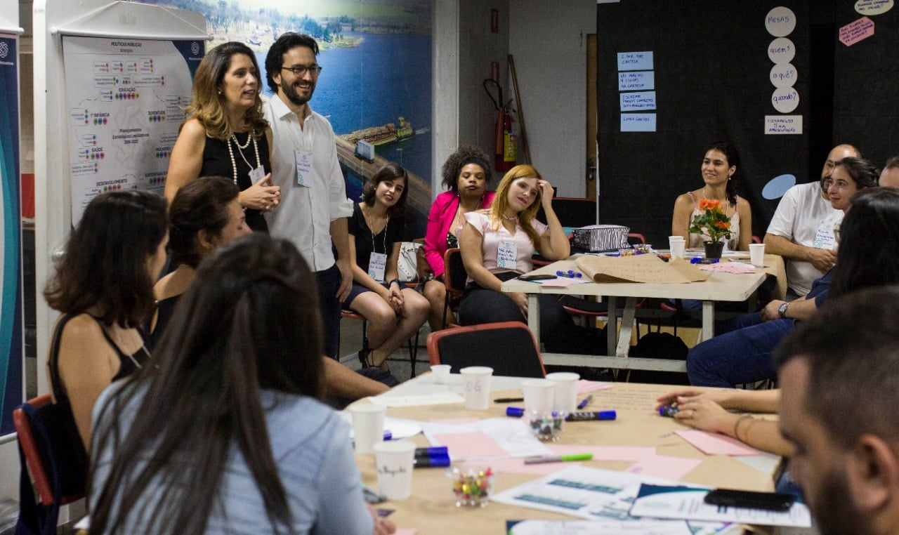 Foto de divulgação do Projeto Mandato Ativo.  Ana Paula (de pé à esquerda) e o André (ao lado dela) falam com parlamentares que participaram do evento na Alesp.