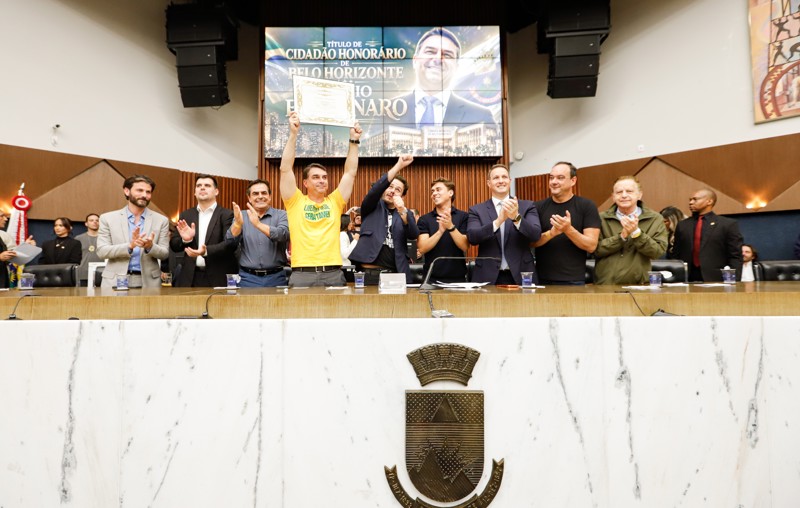 Ao lado de aliados e sob protestos, Flávio Bolsonaro recebe título de cidadão honorário da capital mineira.