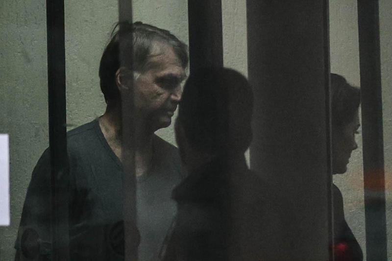 Ex-presidente Jair Bolsonaro é visto através do vidro da sede da Polícia Federal.